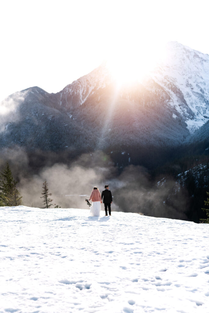 bride and groom walk through snow towards sunsetting behind mountain