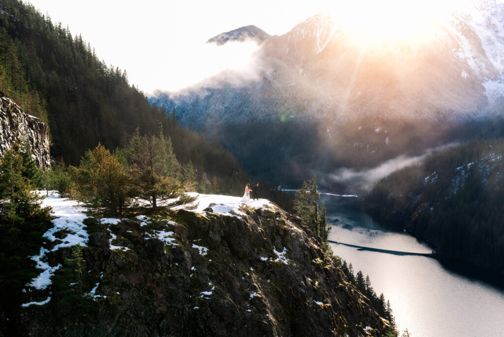 couple atop a snowy cliffside with sunsetting over mountain