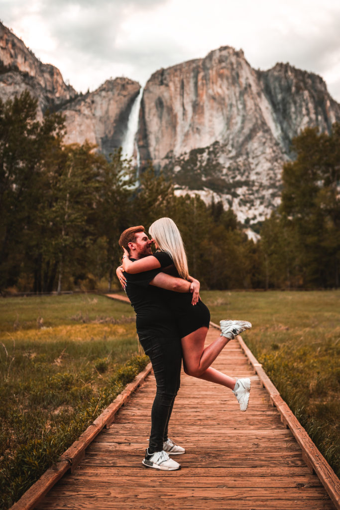 Couple holding each other in nature with mountain and waterfall in background