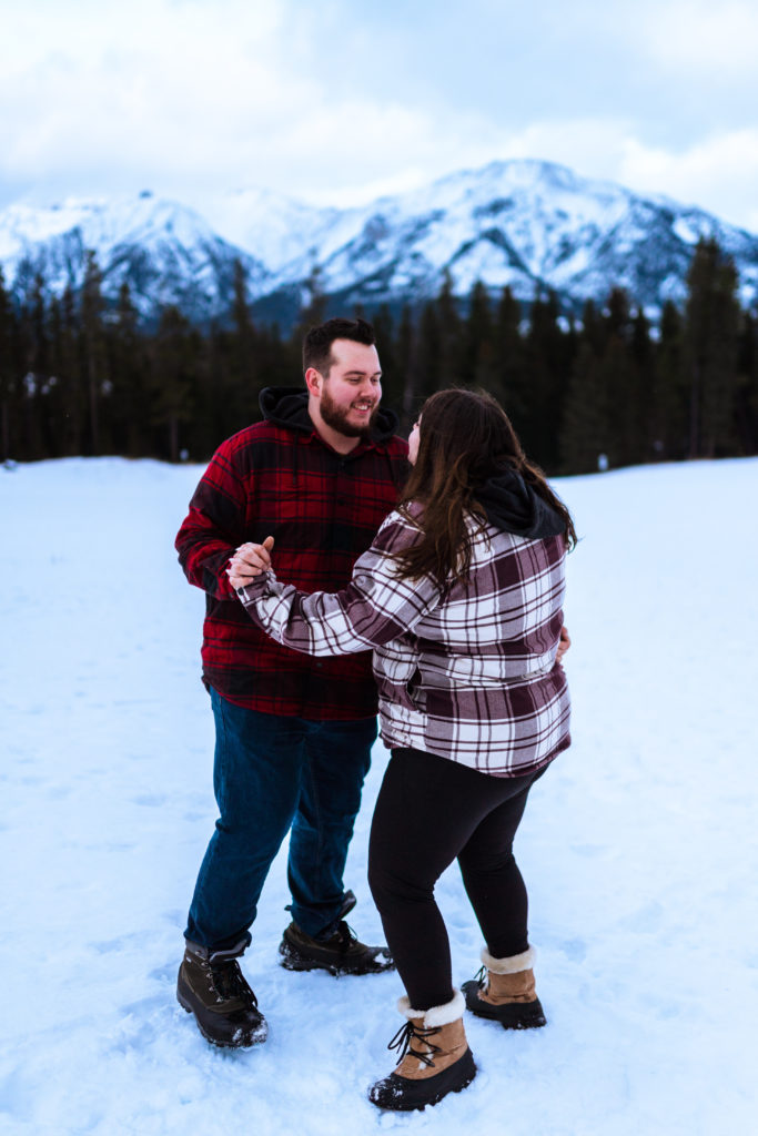 couple wearing red flannel dancing in the snow for engagement session