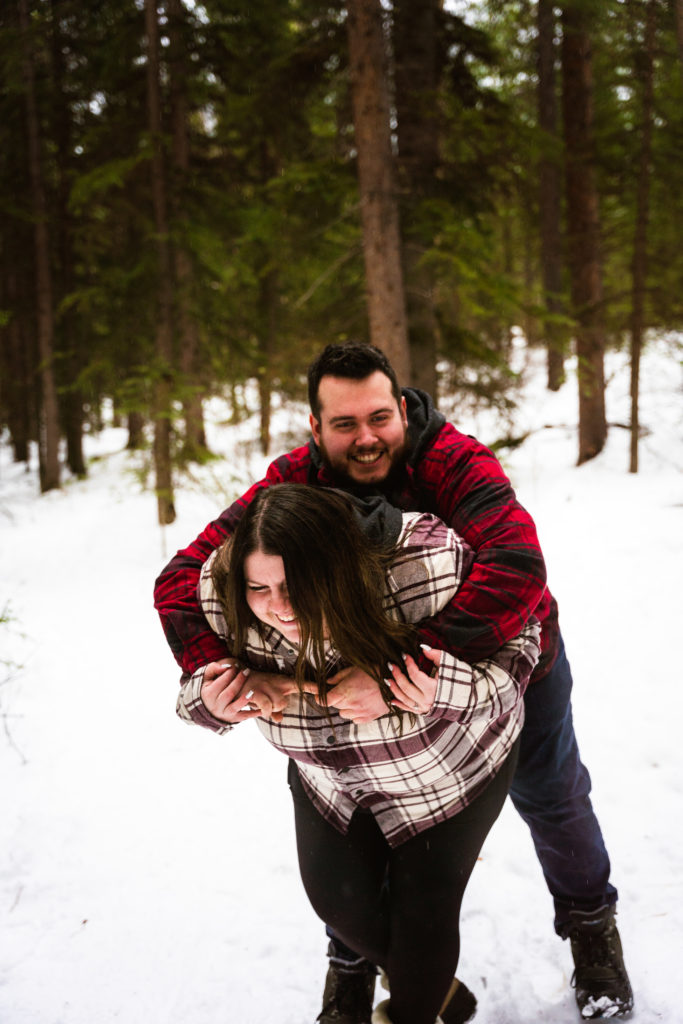 couple laughing during engagement photography session in the snowy forest