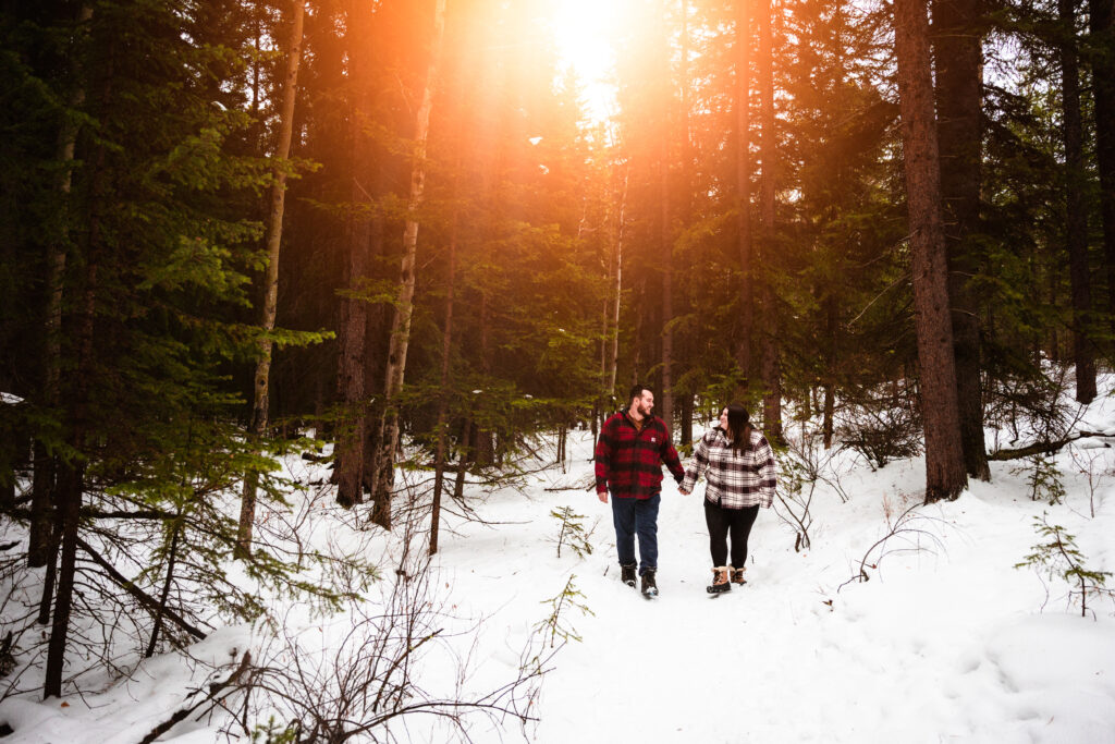 couple walk hand in hand during engagement session in snowy Canmore forest
